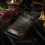 Dark Romance wedding invitation on a phone screen on black velvet, between brass candlesticks and dark roses