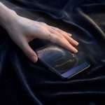 A hand resting on a phone showing the Midnight Celestial wedding invitation, on navy velvet