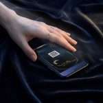 A hand resting on a phone showing the Midnight Celestial RSVP with its QR reply code, on navy velvet