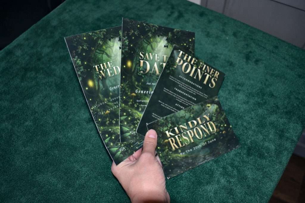 A hand holding four printed pieces from an Enchanted Forest wedding stationery suite