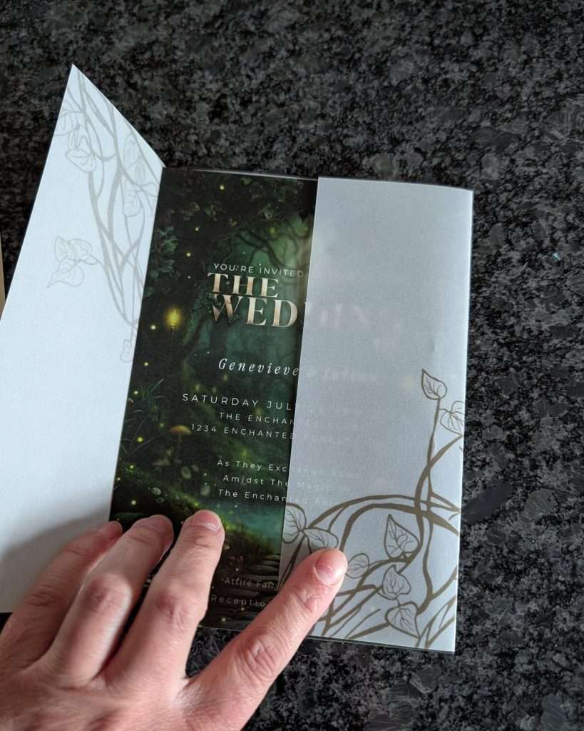 Hand opening a hand-drawn ivy vellum wrap over an Enchanted Forest wedding invitation, alternate view