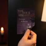 A hand peeling the corner of a Dark Romance 5x7 save the date magnet from a dark fridge door