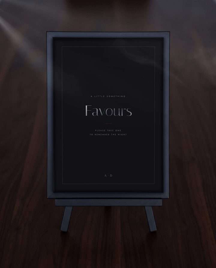 The Obsidian Vow favours sign in a black frame on a small easel, on a dark wood table
