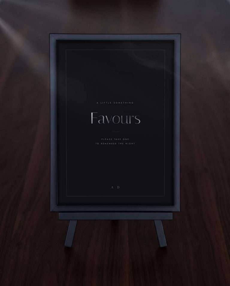 The Obsidian Vow favours sign in a black frame on a small easel, on a dark wood table