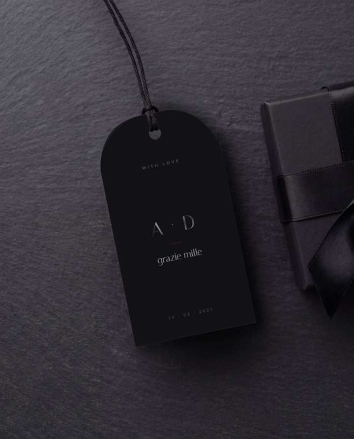 An Obsidian Vow favor tag on black cord, resting on slate beside a ribboned gift