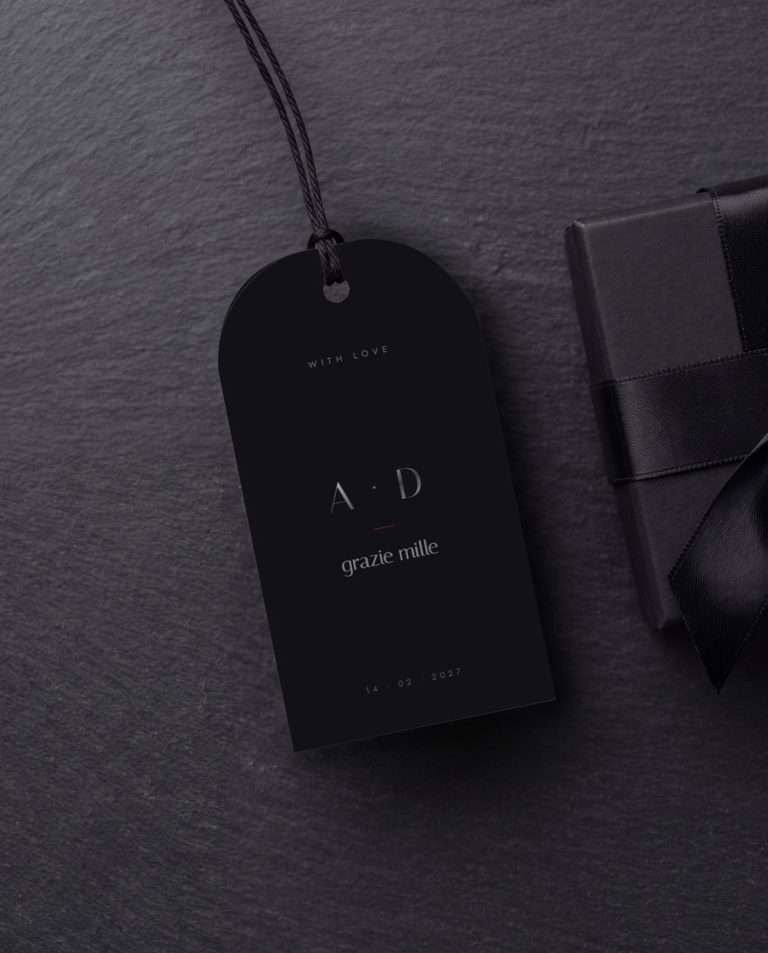 An Obsidian Vow favor tag on black cord, resting on slate beside a ribboned gift