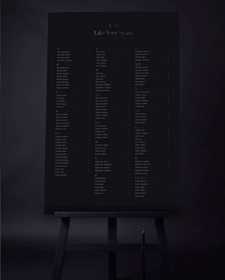 The 24 by 36 Obsidian Vow seating chart on a black easel, Take Your Seats above the guest names set alphabetically in three columns