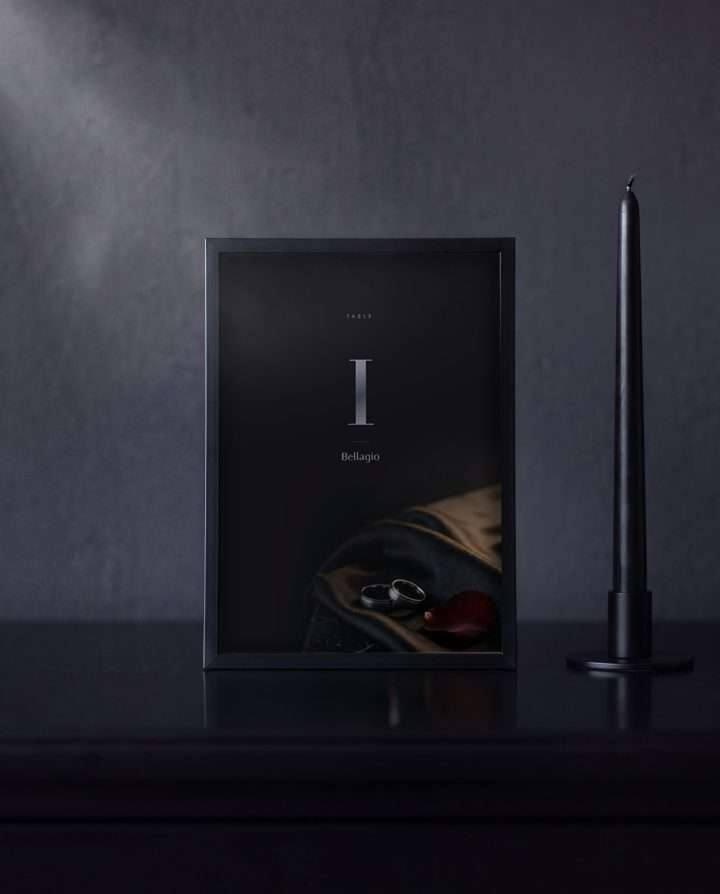 An Obsidian Vow table number in a black frame on a dark sideboard, a black taper candle beside it