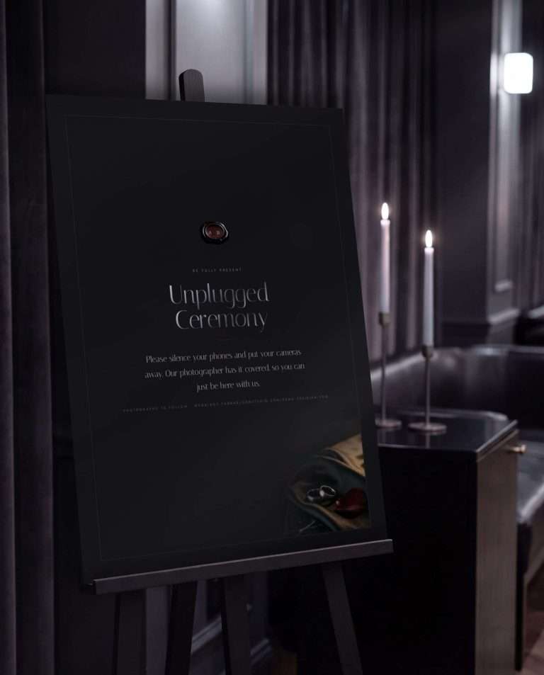 The 18 by 24 Obsidian Vow unplugged ceremony sign on a black easel in a candlelit room, a deep wine wax seal above the words