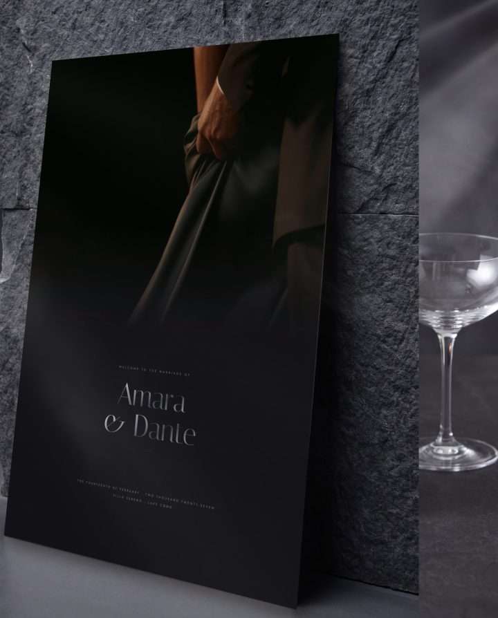 The 24 by 36 Obsidian Vow welcome sign leaning against a dark stone wall, a coupe glass beside it
