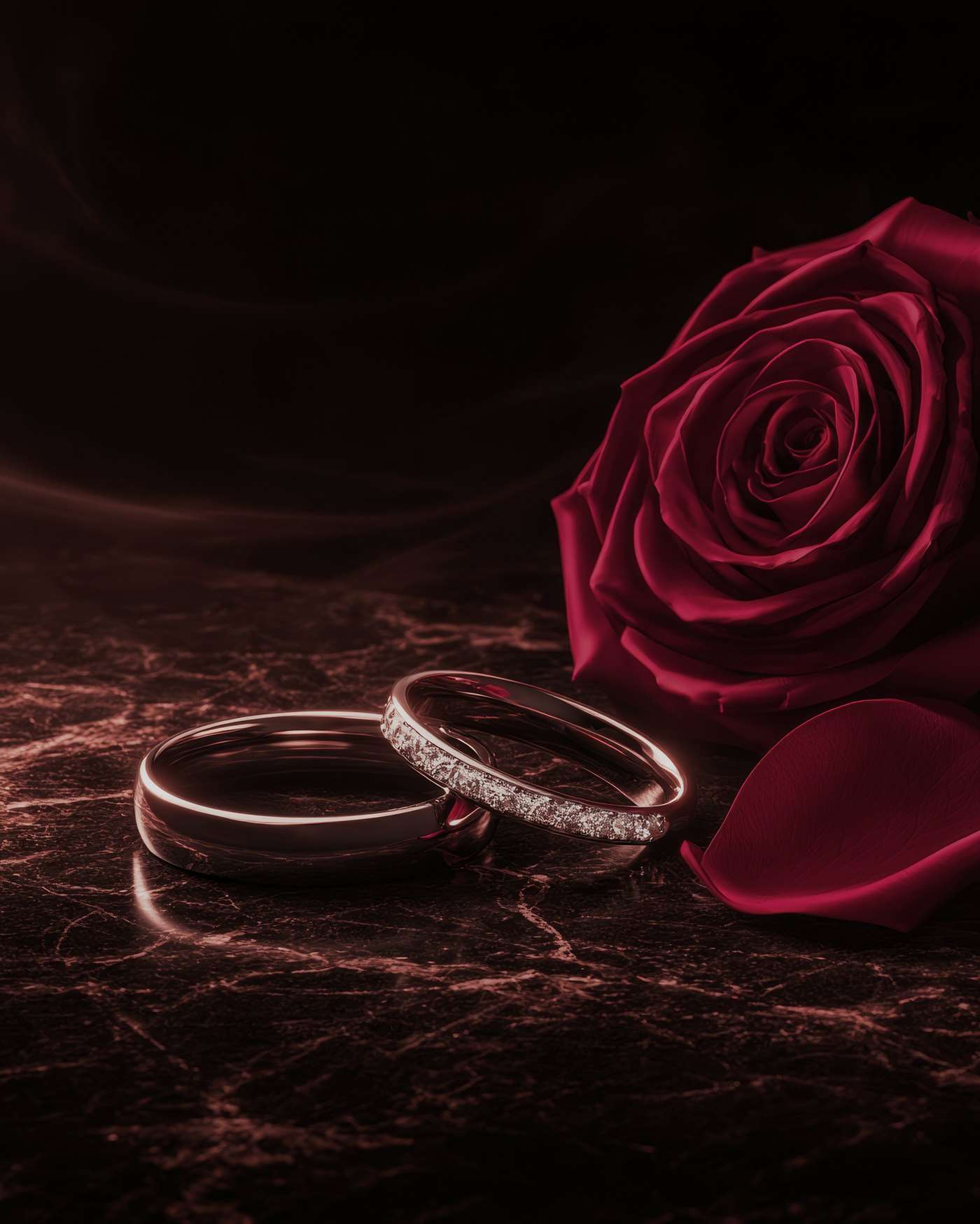 Two wedding rings beside a single deep-red rose on veined dark marble